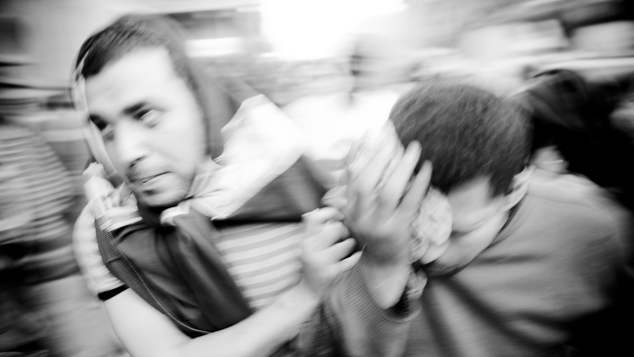 تظهر الصورة رجالاً يتجهون بسرعة في مشهد مزدحم، حيث يبدو أنهم في حالة من الحركة العفوية. الملابس التي يرتدونها متنوعة، ومن الواضح أن هناك نوعاً من التوتر أو الاضطراب في الوضع. الخلفية غير واضحة بسبب الضبابية، مما يعكس شعوراً بالسرعة أو الارتباك. الأربعاء وشعاراتهم تظهر تشويشاً في المشهد، مما يضيف إلى الديناميكية العامة للصورة.