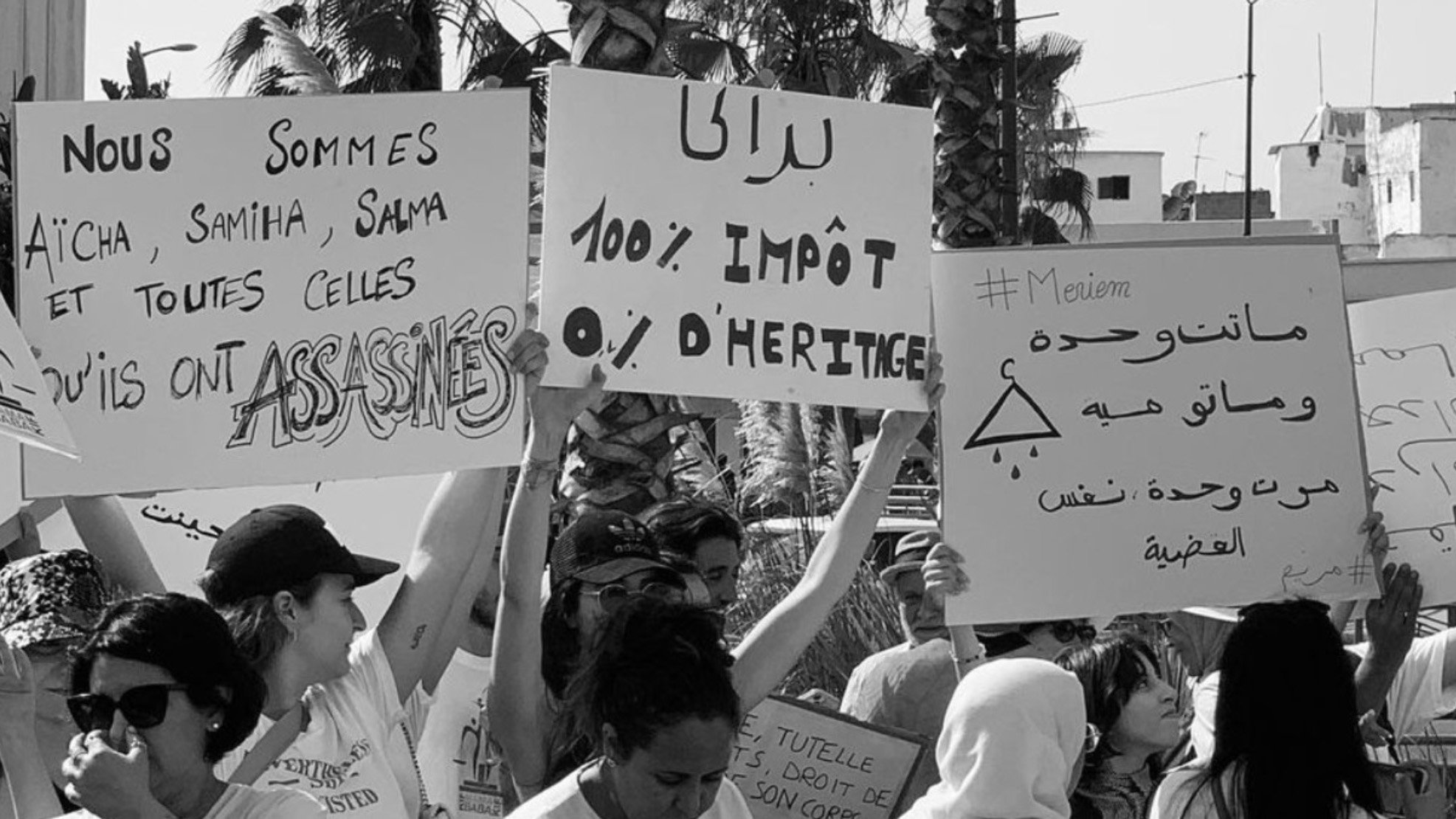 الصورة تظهر مجموعة من الأشخاص يحملون لافتات في مظاهرة. اللافتات تتضمن عبارات تتعلق بالعدالة والحقوق. من بينها نصوص تشير إلى الأحكام الضريبية والمطالبة بالعدالة للضحايا، مما يعكس موقفًا اجتماعيًا أو سياسيًا. الأجواء تبدو حماسية مع حضور العديد من المشاركين.