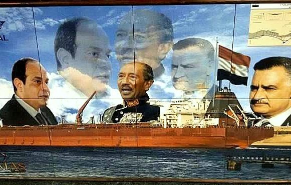 الصورة تُظهر لوحة فنية تتضمن عدة شخصيات تاريخية معروفة، وهي مرتبطة بقناة السويس. في الوسط يظهر سفينة ضخمة تبحر، محاطة بصور لعدد من الشخصيات التاريخية، ربما تعكس مراحل مختلفة من تاريخ مصر والقرارات التي اتُخذت بشأن القناة. الخلفية تحتوي على ملامح من البحر، مما يضيف إلى السياق البحري. اللوحة تعبر عن الفخر الوطني والتاريخ البحري لمصر.