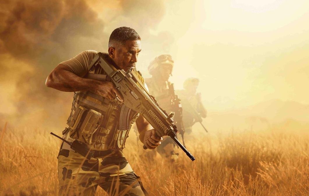 تظهر الصورة مشهدًا عسكريًا في بيئة صحراوية أو مفتوحة. يُرى في المقدمة رجل يرتدي زيًا عسكريًا ويحمل سلاحًا، يبدو مركزًا وجادًا. في الخلفية، يظهر عدد من الجنود الآخرين يتقدمون معه، مما يعزز الإحساس بالتعاون والعمل الجماعي. السماء تمتزج بألوان دافئة، مما يضيف جوًا من التوتر والحركة.