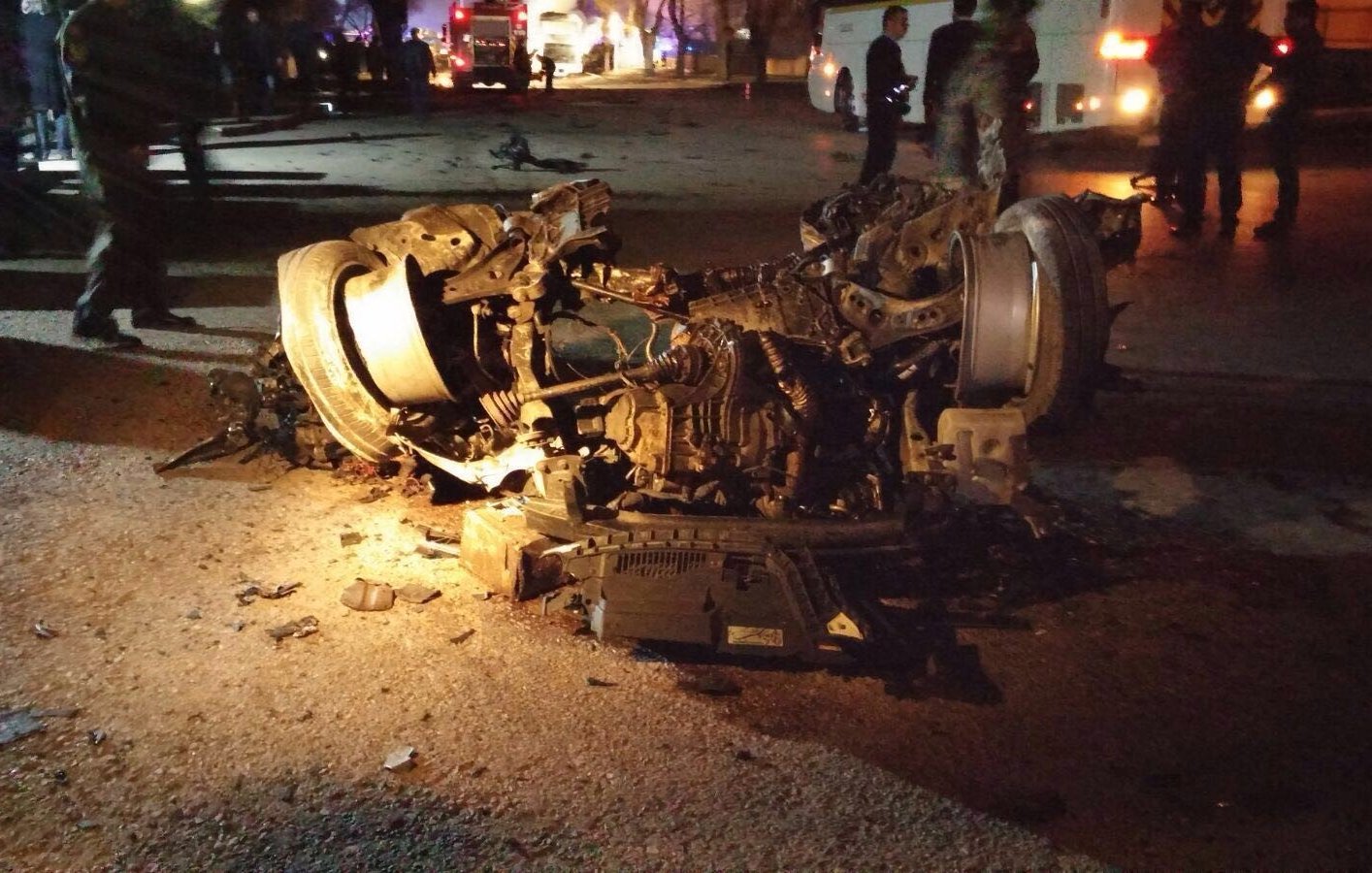 تظهر الصورة حادث سير خطير، حيث تكون السيارة مقلوبة على جانبها، وتبدو الأضرار كبيرة. يمكن رؤية أجزاء من السيارة مألوفة مثل العجلات والمكونات الداخلية، مع تشوهات واضحة نتيجة الاصطدام. الإضاءة خافتة، مما يدل على أن الحادث قد وقع في الليل. يبدو أن هناك أشخاصًا في الخلفية، ربما من فرق الطوارئ أو المتفرجين. الصورة تنقل إحساسًا بالكارثة والخطورة.