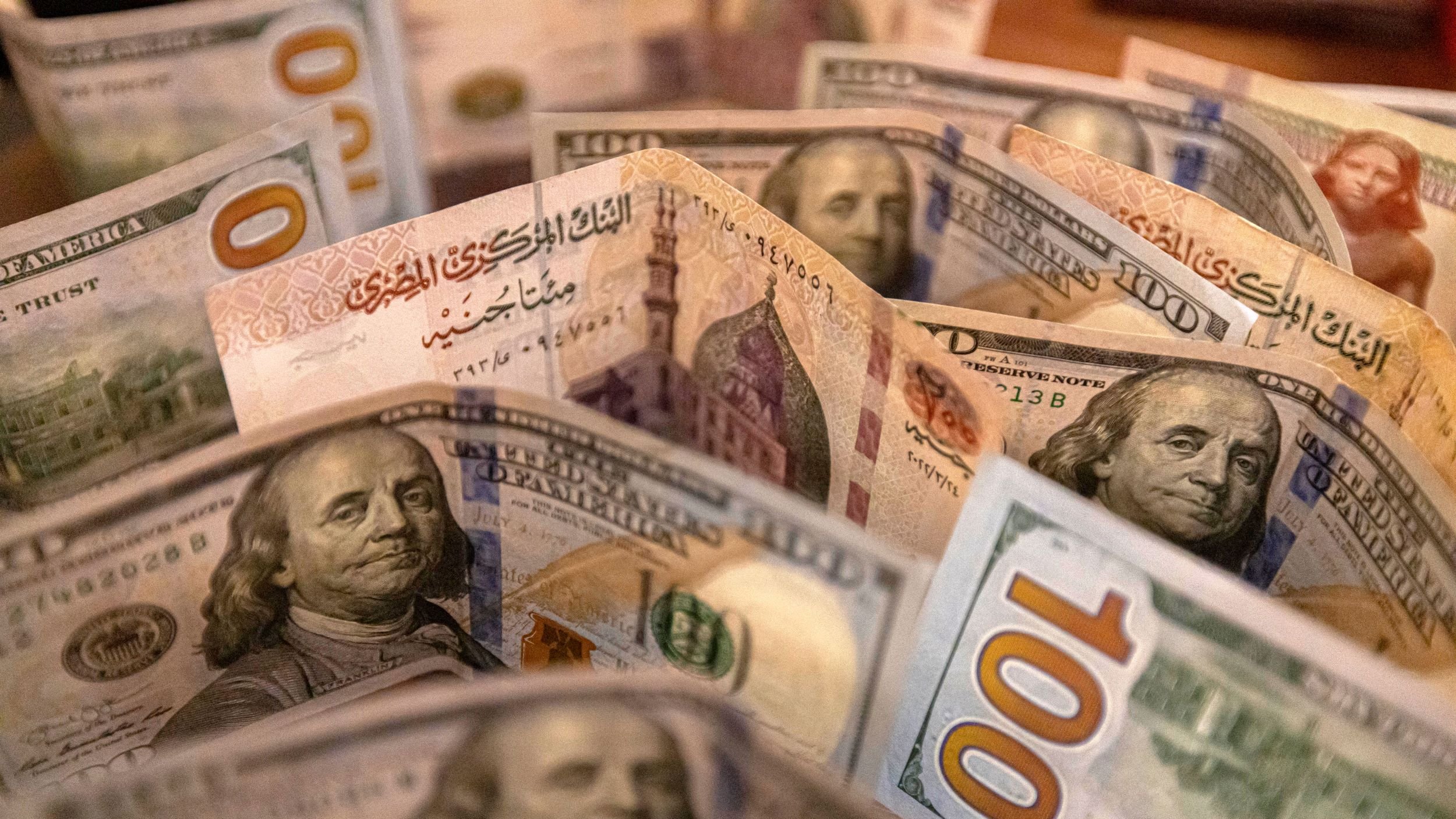 تظهر الصورة مجموعة من الأوراق النقدية الأمريكية من فئة المئة دولار. تتوزع الأوراق بشكل متقارب، مع ظهور وجه بنيامين فرانكلين على الأوراق. الخلفية تشير إلى تفاصيل أخرى، مما يضفي عمقًا للصورة. الألوان بارزة وواضحة، مما يجعل الأوراق النقدية تبدو جديدة وجذابة.
