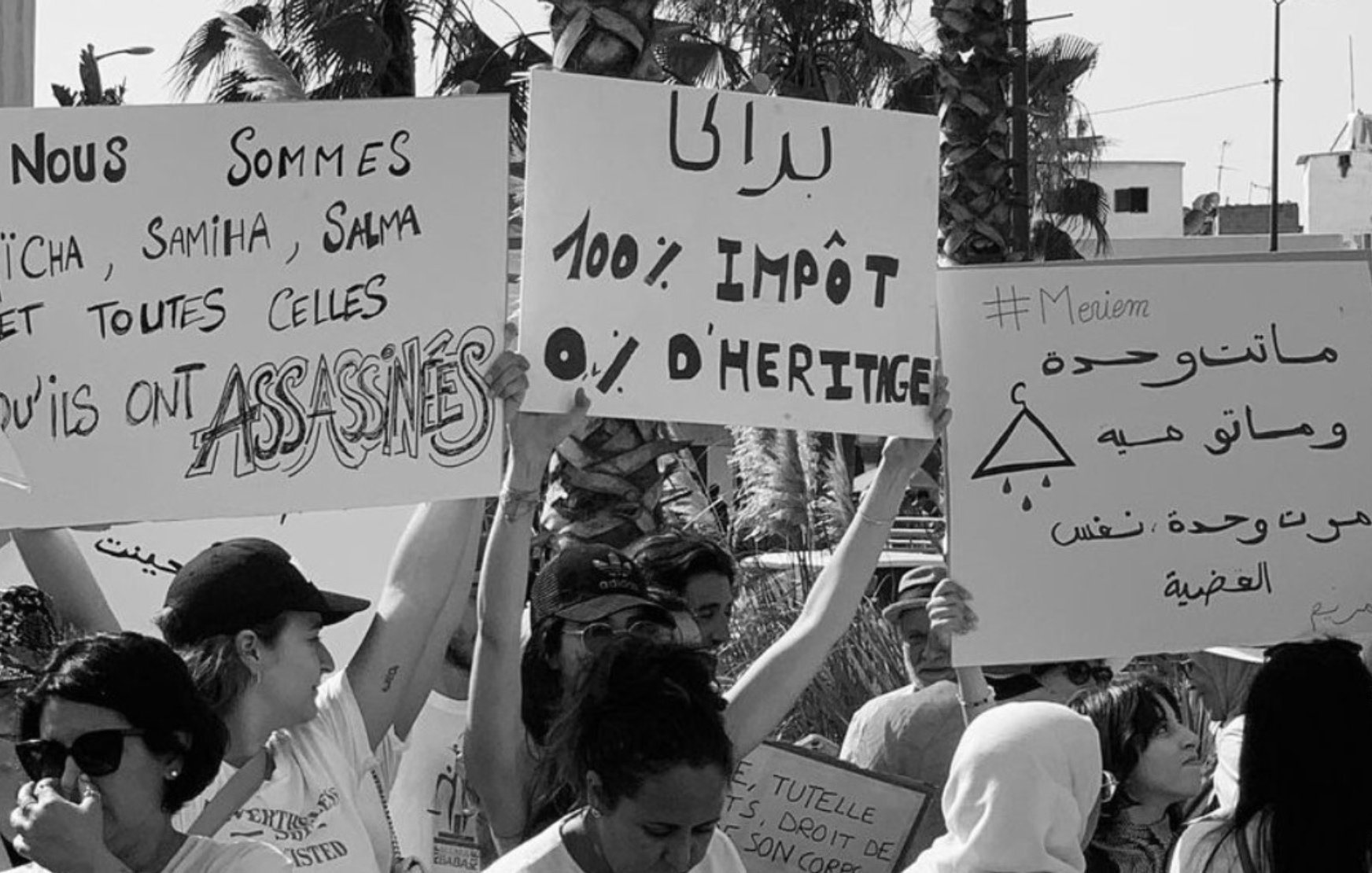 الصورة تظهر مجموعة من الأشخاص يحملون لافتات في مظاهرة. اللافتات تتضمن عبارات تتعلق بالعدالة والحقوق. من بينها نصوص تشير إلى الأحكام الضريبية والمطالبة بالعدالة للضحايا، مما يعكس موقفًا اجتماعيًا أو سياسيًا. الأجواء تبدو حماسية مع حضور العديد من المشاركين.