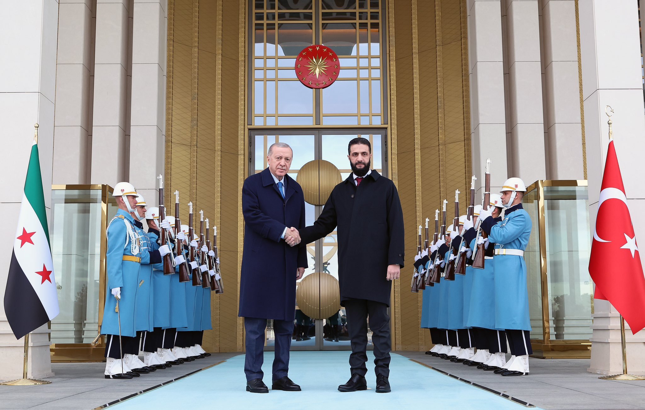 الصورة تُظهر شخصين يتصافحان أمام مدخل فخم، حيث يقف الجنود في الخلفية في تنسيق دقيق. الأجواء رسمية وتعكس حدثاً مهماً.