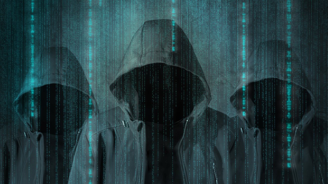 الصورة تظهر ثلاثة أشخاص يرتدون هوديات (أغطية رأس) سوداء، وجوههم غير مرئية. خلفهم يوجد تدرجات من الألوان الزرقاء تشبه البيانات الرقمية المتساقطة، مما يعطي انطباعًا عن بيئة إلكترونية أو تكنولوجية. الأجواء العامة للصورة توحي بالغموض أو الإخفاء.