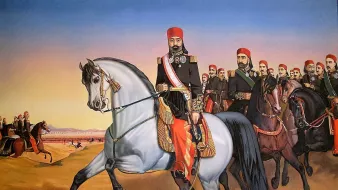 تظهر في الصورة مجموعة من الفرسان، حيث يتقدمهم قائد على حصان أبيض. يرتدي القائد زيًا تقليديًا مزينًا بالألوان الزاهية والأوسمة، مما يدل على مكانته العالية. خلفه، يظهر مجموعة من الفرسان الآخرين الذين يرتدون أيضًا ملابس تقليدية. يتسم المشهد بهدوء السماء وألوان دافئة، مما يضفي شعورًا بالفخر والاعتزاز. تعكس الصورة الروح العسكرية والفخر بالتراث.