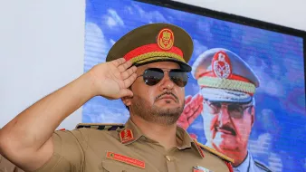 ضابط عسكري يرتدي زيًا رسميًا ونظارات شمسية، يؤدي تحية عسكرية.