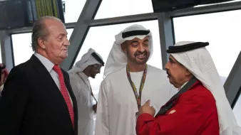 في الصورة، يظهر ثلاثة رجال يتحدثون معًا. يرتدي أحدهم بدلة رسمية، بينما يرتدي الآخرون الملابس التقليدية العربية. الخلفية تحتوي على شاشات عرض لمعلومات الطيران. يبدو أن الحديث يجري في مكان رسمي، مثل مطار أو مركز اجتماعات. الجو العام يوحي بالتقارب والتفاعل الودي بين الأشخاص.