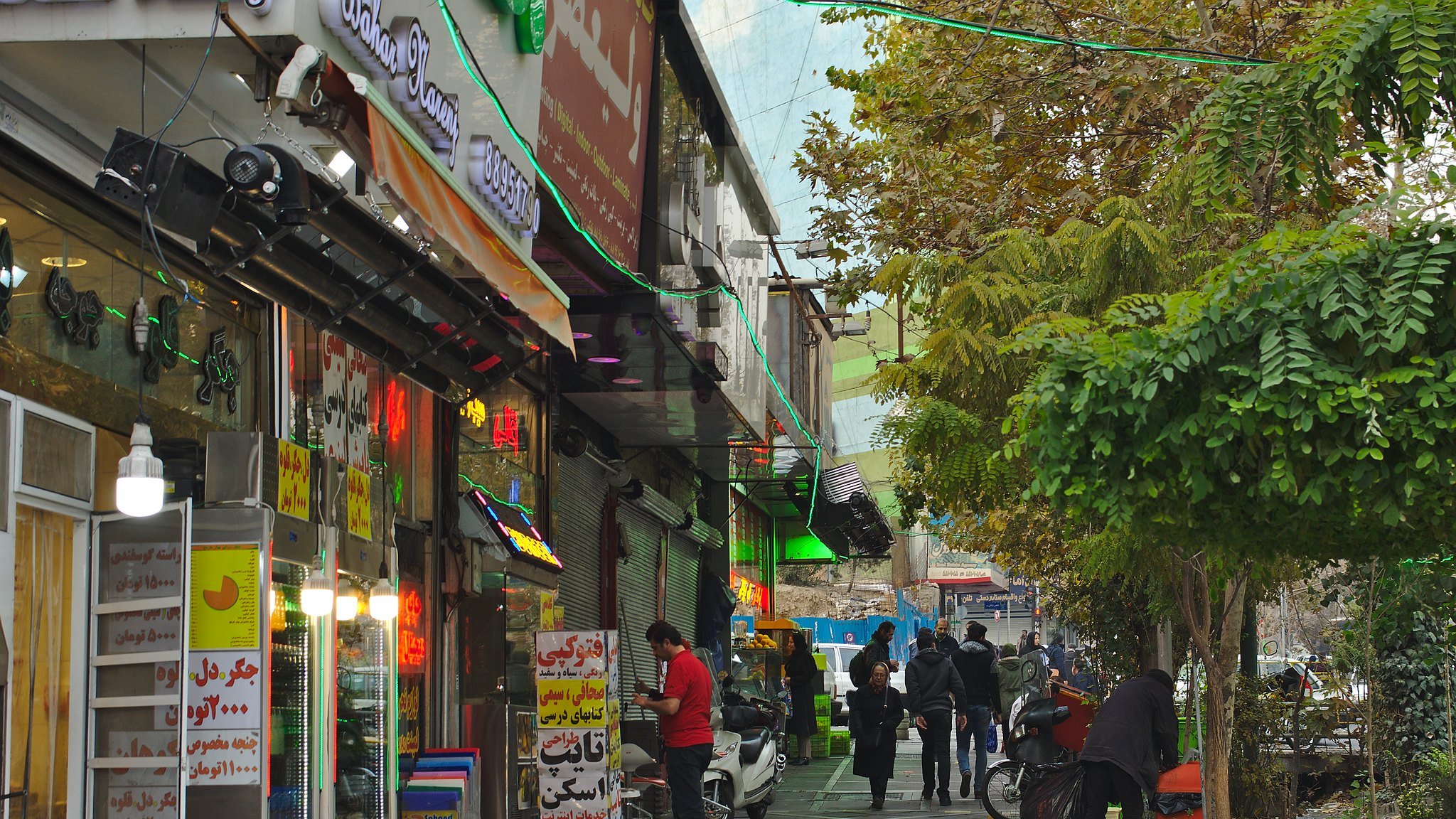 A bustling street lined with shops, colorful signs, and people walking along the pavement.