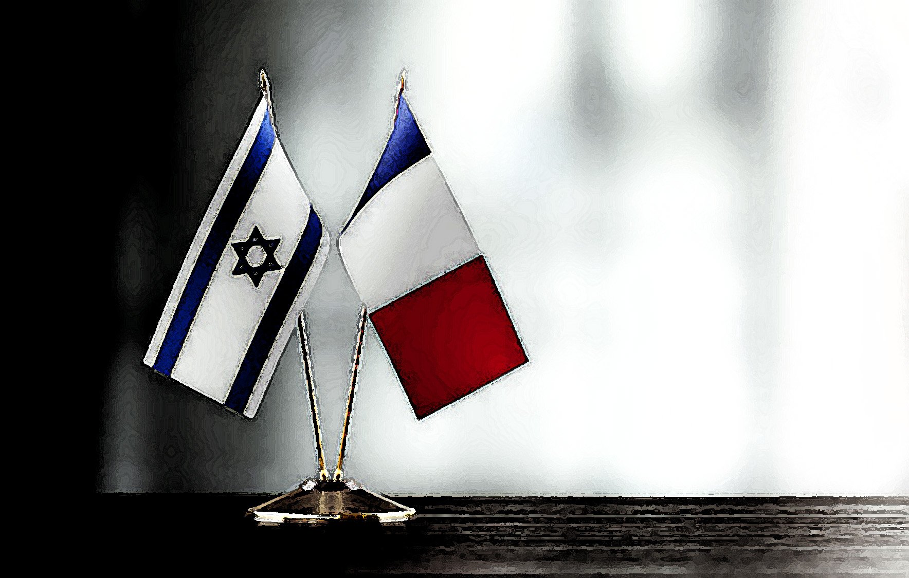 The image features two small flags positioned on a surface. One flag is the national flag of Israel, characterized by its blue and white colors and a Star of David in the center. The other flag is the national flag of France, which consists of three vertical stripes: blue, white, and red. The flags are mounted on small stands, standing together side by side, against a softly blurred background.