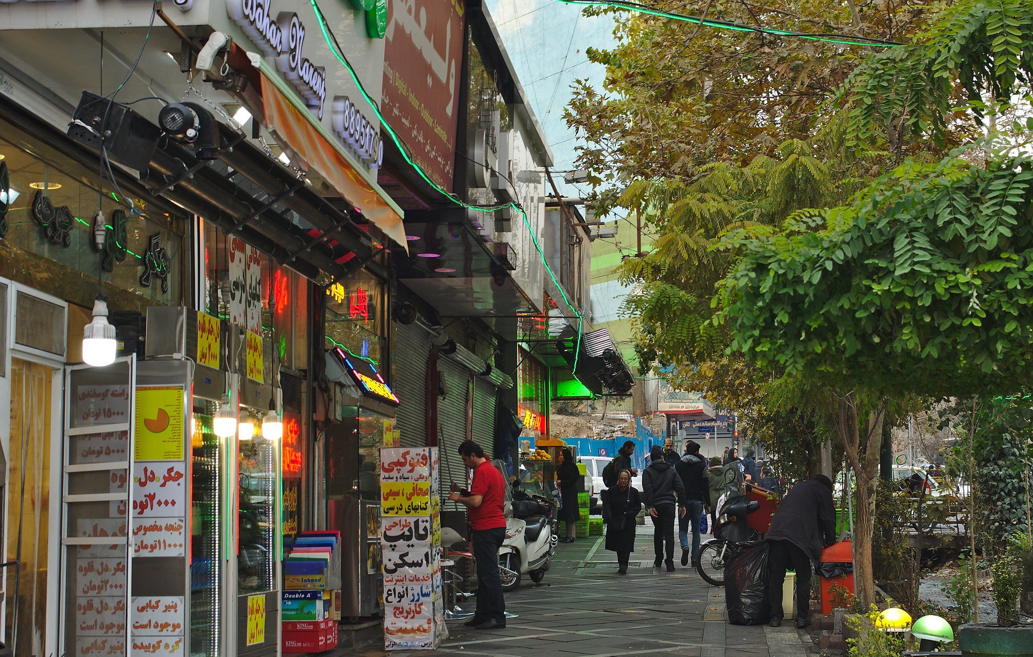 A bustling street lined with shops, colorful signs, and people walking along the pavement.