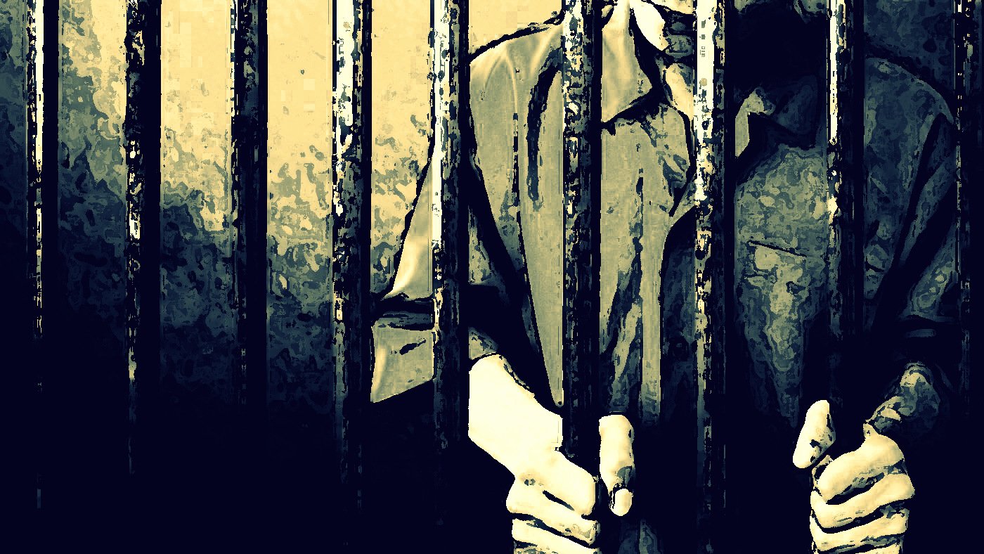 The image depicts a person standing behind bars, likely in a prison setting. The figure appears to be gripping the bars with both hands, suggesting a feeling of confinement. The scene is characterized by shadowy lighting and a muted color palette, creating an atmosphere of isolation and despair. The focus is primarily on the hands and the bars, emphasizing the sense of imprisonment.