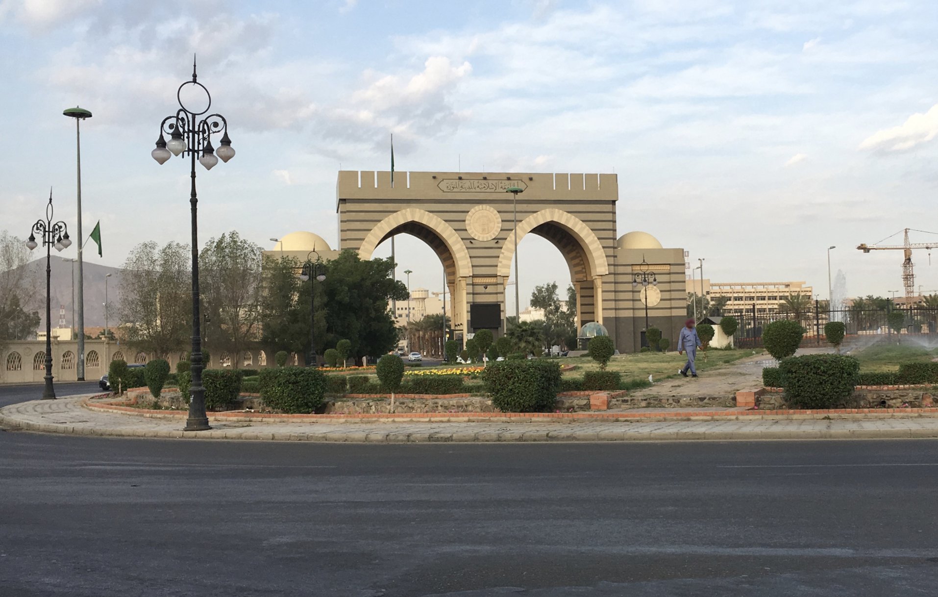 A large archway with decorative towers, surrounded by greenery and a road.
