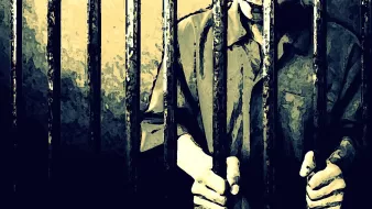 The image depicts a person standing behind bars, likely in a prison setting. The figure appears to be gripping the bars with both hands, suggesting a feeling of confinement. The scene is characterized by shadowy lighting and a muted color palette, creating an atmosphere of isolation and despair. The focus is primarily on the hands and the bars, emphasizing the sense of imprisonment.