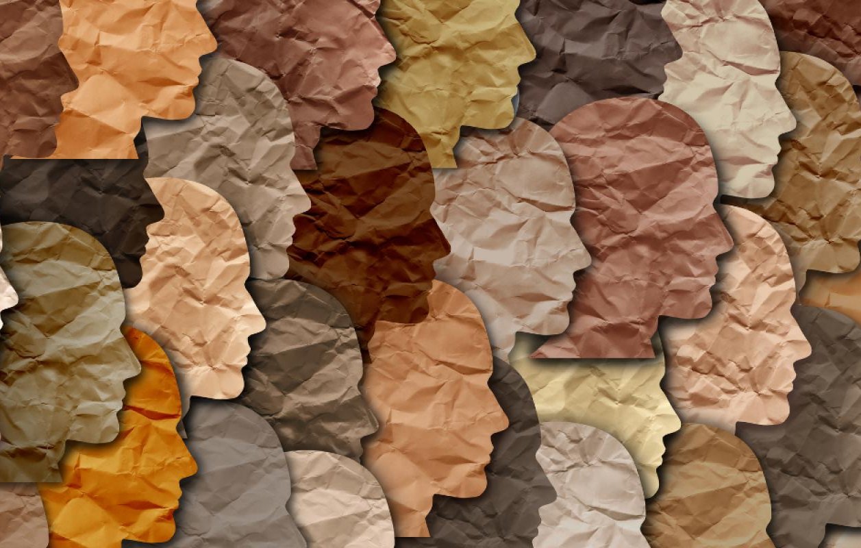 La imagen presenta una composición de siluetas de rostros en diferentes tonos de color. Las siluetas están organizadas de manera que se superponen y se integran entre sí, creando un efecto visual interesante. Los colores varían desde tonos claros hasta oscuros, y la textura del papel arrugado añade profundidad a la imagen. Esta representación puede simbolizar la diversidad y la variedad de identidades.
