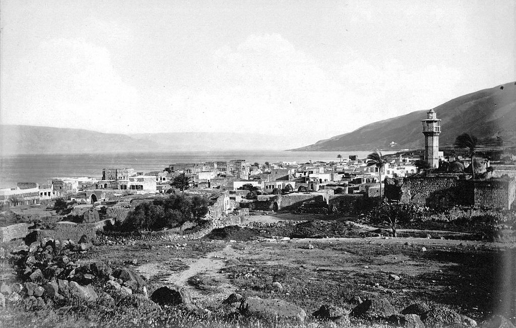 این تصویر نمایشدهنده یک مناظر تاریخی از یک روستا یا شهر نزدیک به دریاچه است. در تصویر، یک برج باستانی در سمت راست دیده میشود که به واسطه آن، هویت محلی خاصی به چشم میآید. ساختمانها در سمت چپ و در پسزمینه قرار دارند و برخی از آنها به نظر میرسد که با مصالح سنگی ساخته شدهاند. در دوردست، کوهها و زمینهای مرتفع قابل مشاهدهاند و ابرها در آسمان پراکندهاند. به طور کلی، این تصویر حس تاریخ و طبیعت آرام را به بیننده منتقل میکند.