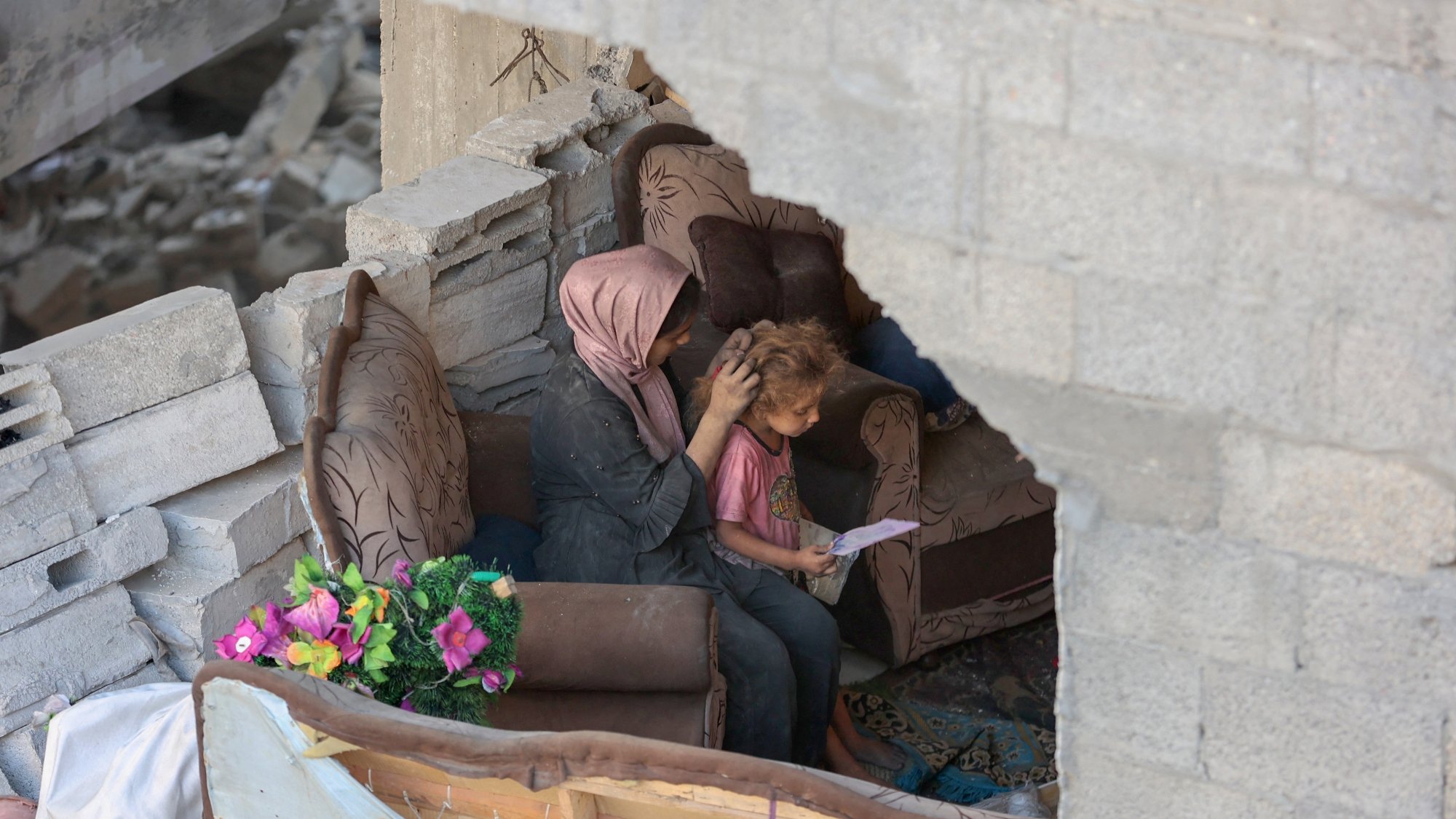 مادری بر روی مبل خراب نشسته و موهای کودک را نوازش میکند. در پسزمینه، ویرانی مشهود است.