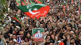 تصویر نشاندهندهی تجمع بزرگ مردمی است که در یک رویداد سیاسی شرکت کردهاند. افراد در این جمعیت با پرچمها و شعارهای مختلف از یک شخصیت سیاسی حمایت میکنند. برخی از آنها تصاویر شخص مورد نظر را در دست دارند و به نشانه حمایت، دستهای خود را بالا بردهاند. جو حاکم بر جمع، پرشور و هیجانانگیز به نظر میرسد.