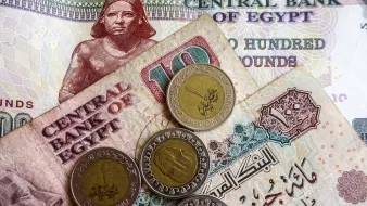 در این تصویر، تعدادی پول نقد مصری به نمایش گذاشته شده است. شامل یک اسکناس ۲۰۰ پوندی و یک اسکناس ۱۰ پوندی که در پسزمینه دیده میشود. همچنین چهار سکه یک پوندی روی اسکناسها قرار دارد. طراحی اسکناسها و سکهها حاوی نقوش و نوشتههایی به زبان عربی است که بیانگر هویت بانک مرکزی مصر و ارزش پولها میباشد. رنگهای مختلف اسکناسها و سکهها به وضوح قابل مشاهده است.