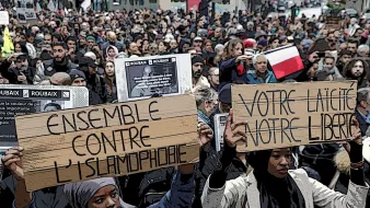 در تصویر، تجمع زیادی از مردم را مشاهده میکنیم که در یک راهپیمایی یا تظاهرات شرکت کردهاند. تعدادی از شرکتکنندگان در حال نگهداشتن تابلوهایی با نوشتههایی به زبان فرانسه هستند. یکی از تابلوها به "بدون اسلامهراسی" اشاره دارد و دیگری به "جدایی و آزادی" اشاره میکند. پوسترهای پشت سر آنها نیز به موضوعات مختلفی اشاره دارند. جو کلی تصویر نشاندهنده اعتراض و ابراز نظر جمعی نسبت به مسائل اجتماعی و سیاسی است.