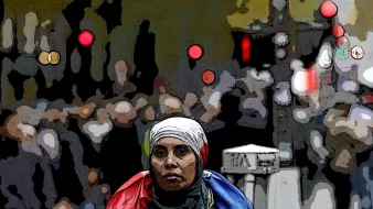 تصویر یک زن را نشان میدهد که به سمت دوربین نگاه میکند و روی دوش او یک پرچم، احتمالاً پرچم فرانسه، قرار دارد. او به نظر میرسد در یک خیابان شلوغ ایستاده است و جمعیتی در پسزمینه دیده میشود. نقاط نورانی و رنگی در پسزمینه به تصویر حس شهری و پویایی میدهند. خانم در تصویر حجاب بر سر دارد و احساس جدیت و تمرکز را منتقل میکند.