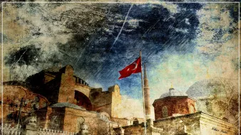 تصویر نشاندهنده یک ساختمان تاریخی با معماری خاص است که به نظر میرسد نمایی از ایاصوفیه (حاجیا صوفیا) در استانبول باشد. در جلو، پرچم ترکیه بر روی ستونی نصب شده و زمینه آسمان با ابرهای غلیظ و رنگی شده است. بافت تصویر به نظر میرسد که دارای افکتهایی است که حس قدیمی بودن و تاریخی بودن را القا میکند. معماری ساختمان با جزئیات زیبایی طراحی شده و فضای کلی تصویر حالتی شاعرانه و تاریخی دارد.