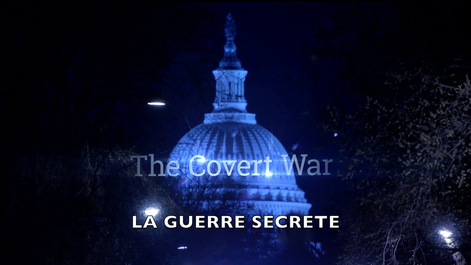 L'image montre un bâtiment emblématique, probablement le Capitole, illuminé de façon dramatique la nuit. En haut de l'image, on peut lire "The Covert War" en lettres blanches, tandis qu'en bas, le texte "LA GUERRE SECRETE" est affiché en plus grand, sur un fond sombre. L'éclairage crée une atmosphère mystérieuse et intrigante, suggérant un thème lié à la clandestinité ou aux opérations secrètes.