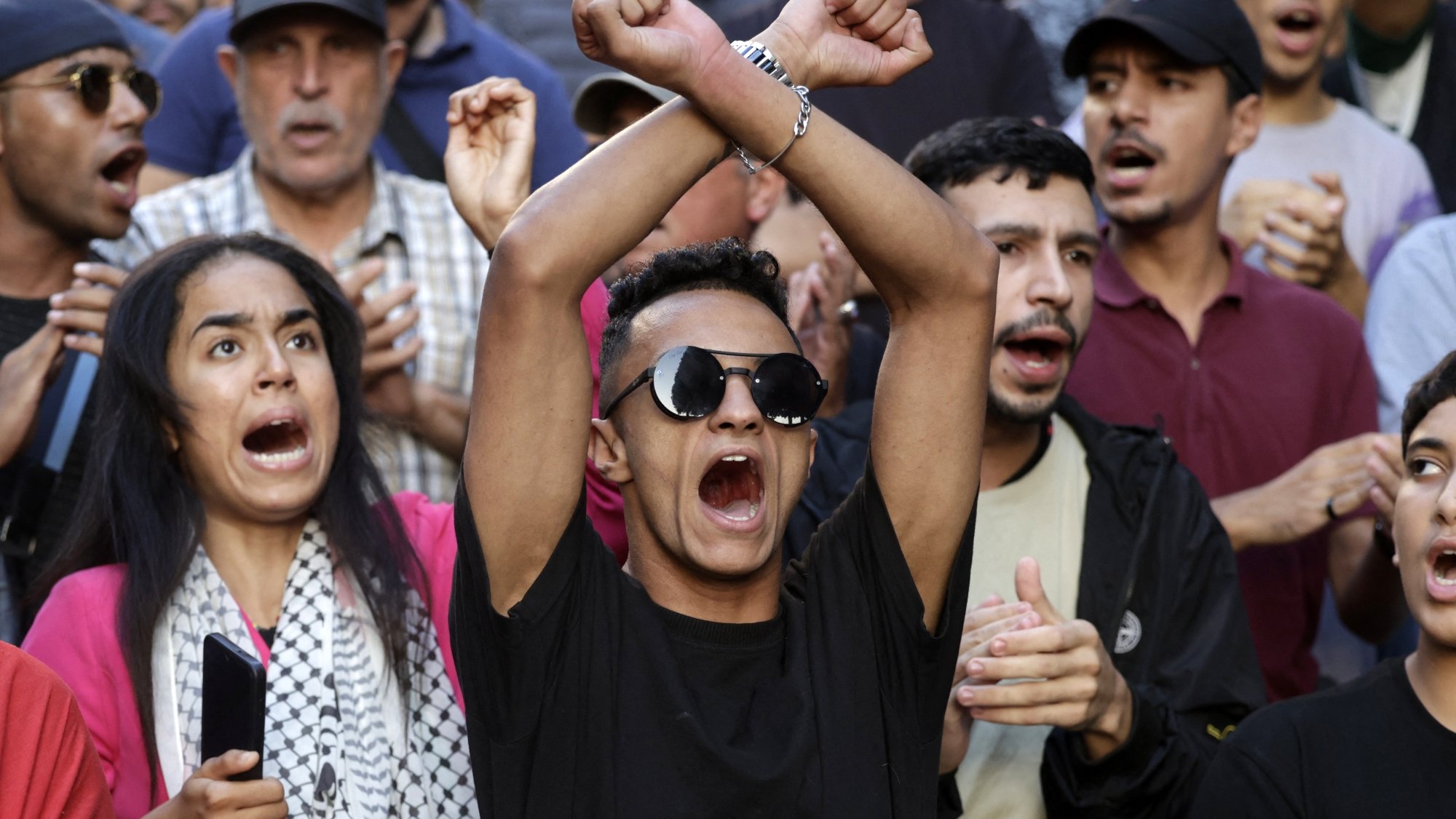 Groupe de manifestants exprimant des émotions fortes, certains brandissant les bras.