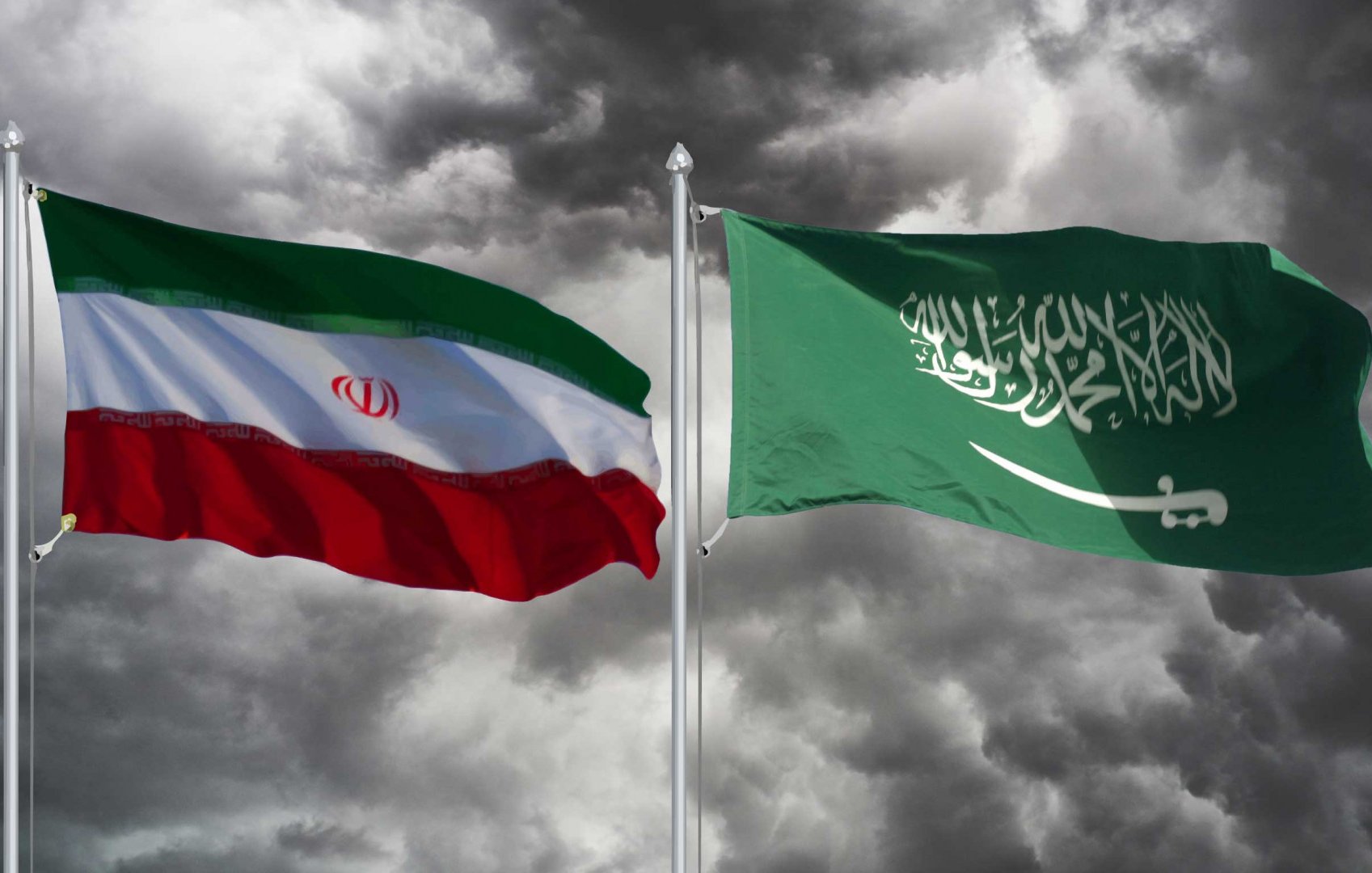 L'image montre deux drapeaux flottant l'un à côté de l'autre. À gauche, le drapeau iranien, qui est composé de bandes horizontales rouges, blanches et vertes, ainsi qu'un insigne en vert. À droite, le drapeau saoudien, qui est principalement vert avec un texte en calligraphie arabe en blanc et une épée en dessous. En arrière-plan, on peut voir des nuages sombres, ce qui crée une ambiance dramatique.