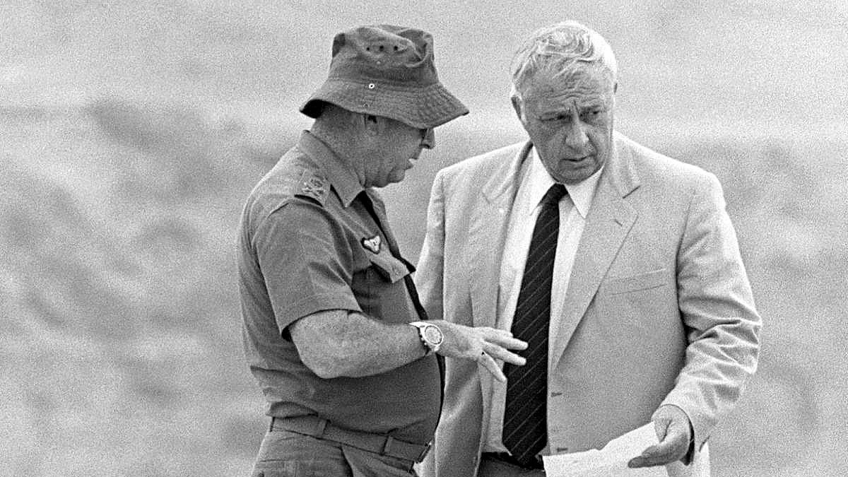 L'image montre deux hommes en train de discuter. L'un d'eux porte une tenue militaire, incluant un chapeau, tandis que l'autre est vêtu d'un costume clair. Ils semblent examiner un document ensemble et échanger des informations de manière sérieuse. L'arrière-plan est flou, suggérant un environnement extérieur. La scène dégage une impression de concentration et d'importance.