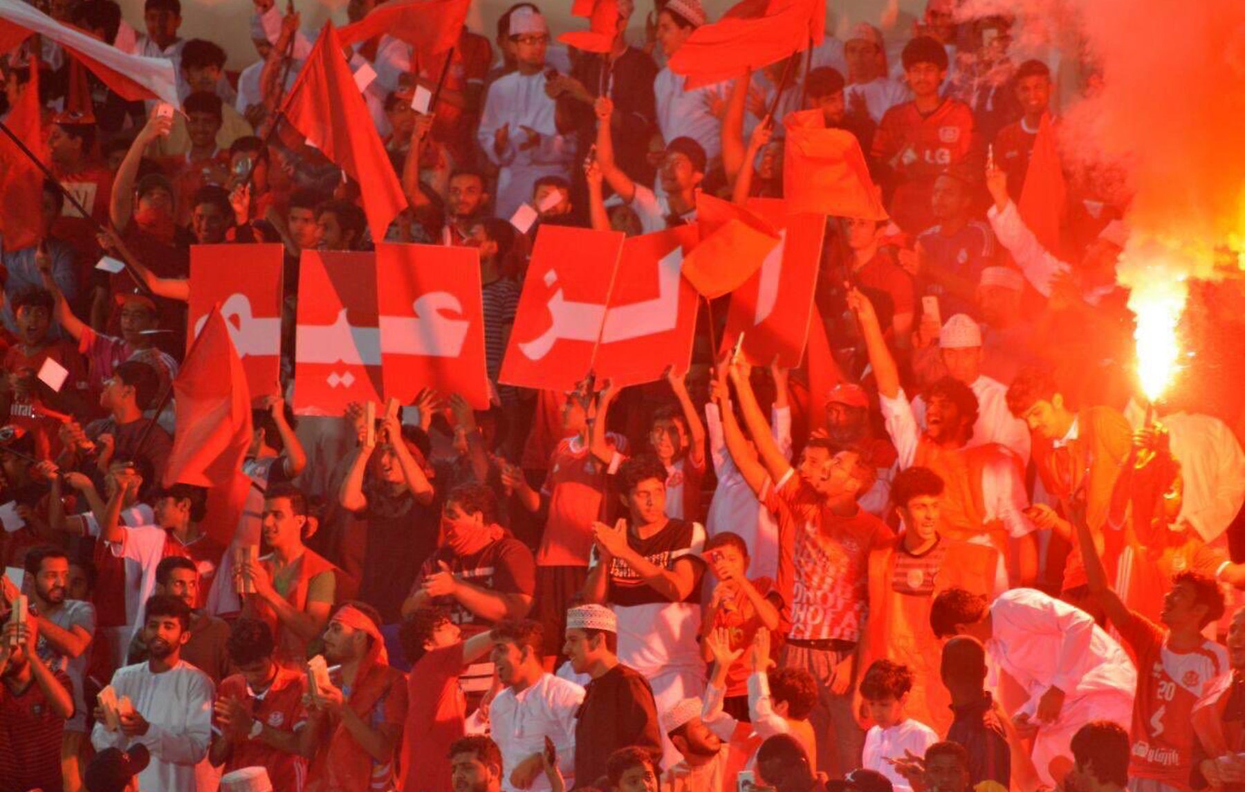 Supporters en fête, agitant des drapeaux rouges et des affichettes dans une ambiance dynamique.