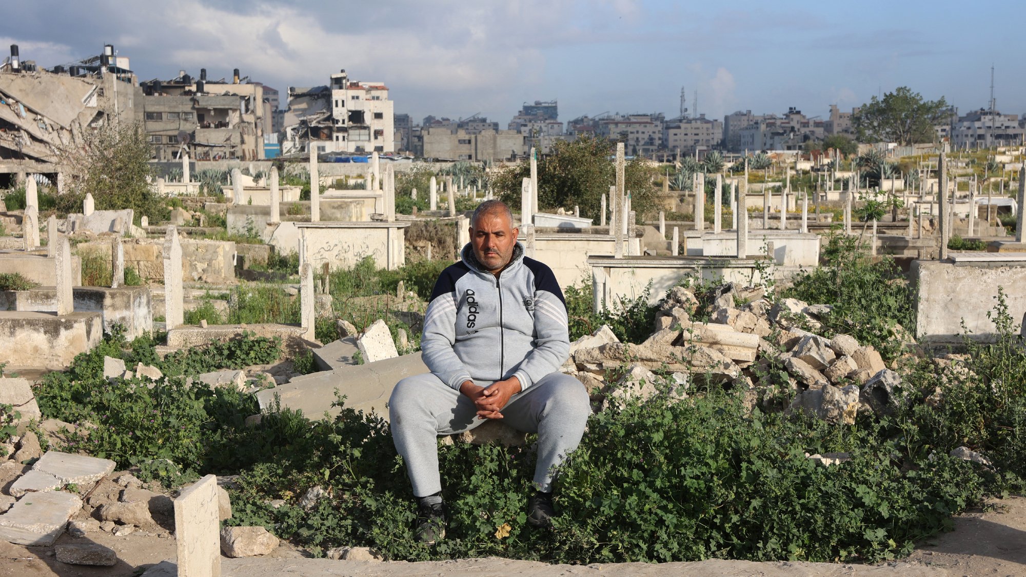 Un homme assis parmi des tombes dans un cimetière, entouré de végétation.
