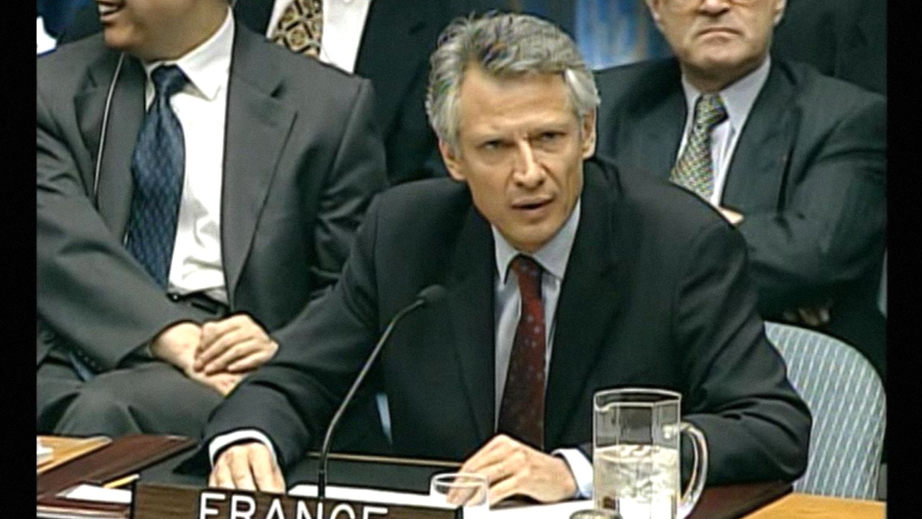 Homme en costume, sérieux, représentant la France lors d'une réunion officielle.
