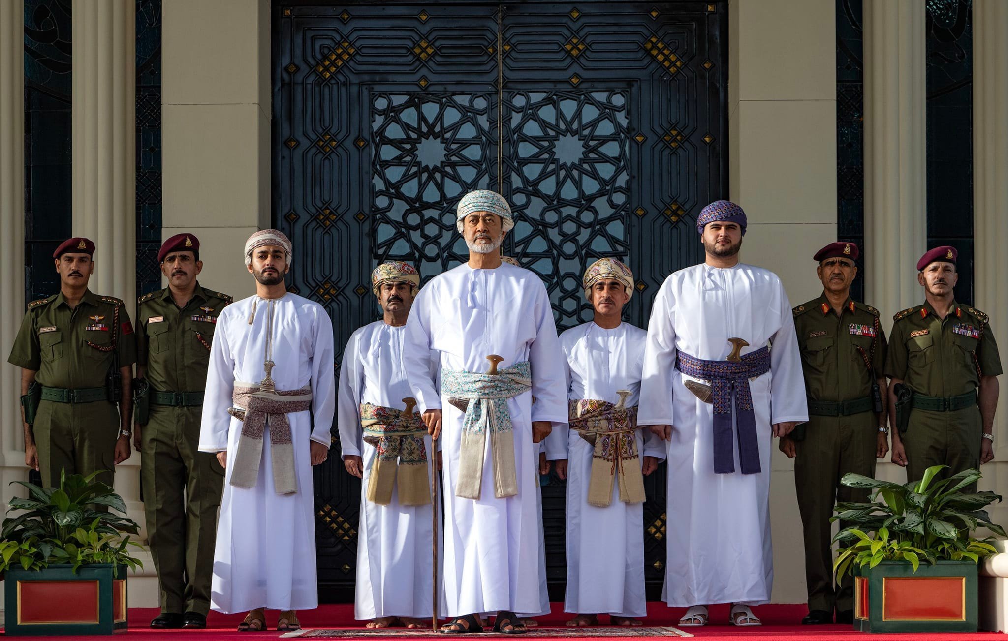Groupe en tenues traditionnelles, debout devant un bâtiment orné, entouré de gardes.