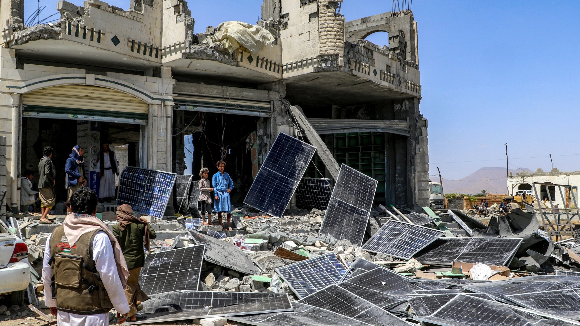 Destruction : bâtiment effondré, débris et panneaux solaires éparpillés autour.