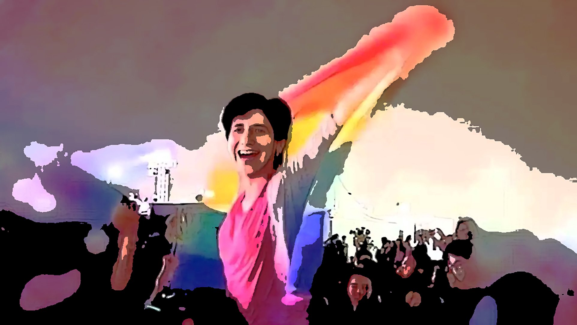 L'image montre une foule enthousiaste lors d'un événement festif, probablement une célébration de fierté. Au premier plan, une personne souriante, drapée d'un grand drapeau aux couleurs arc-en-ciel, lève les bras en signe de joie et de célébration. L'ambiance semble vibrante et festive, avec de nombreuses personnes derrière elle, partageant ce moment de convivialité. Les couleurs vives et l'expression de bonheur contribuent à une atmosphère très positive.