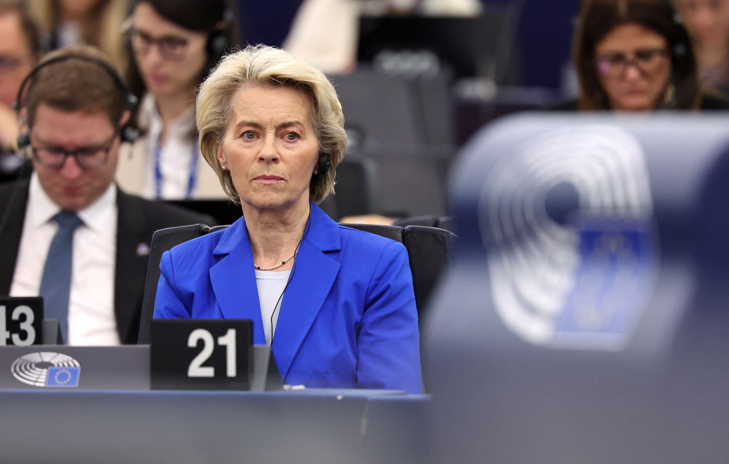 L'image montre une femme assise dans un environnement de réunion, probablement au sein d'une institution européenne, comme le Parlement européen. Elle porte un blazer bleu et semble concentrée sur un sujet abordé lors de la séance. En arrière-plan, on aperçoit d'autres personnes, également attentives. L'atmosphère paraît formelle et sérieuse, et des équipements audio sont visibles, suggérant une translation ou un écoute attentive des débats.