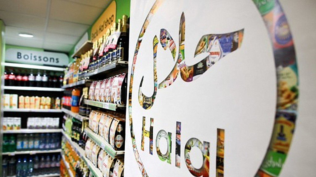 L'image montre une vue intérieure d'un magasin avec une étagère remplie de divers produits alimentaires et boissons. Au premier plan, il y a un grand logo représentant le mot "Halal" en lettres stylisées. Ce logo est intégré dans un design créatif qui semble inclure des images de produits alimentaires. L'éclairage est clair, et l'ambiance générale de la scène est celle d'un espace de vente organisé et vibrant.
