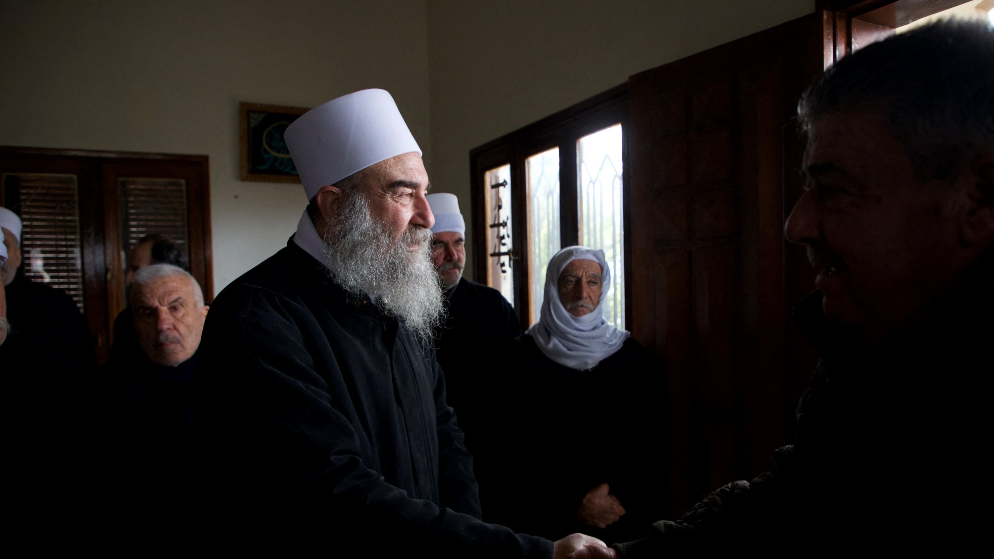 Des hommes en vêtements sombres se serrent la main dans une pièce avec des fenêtres.