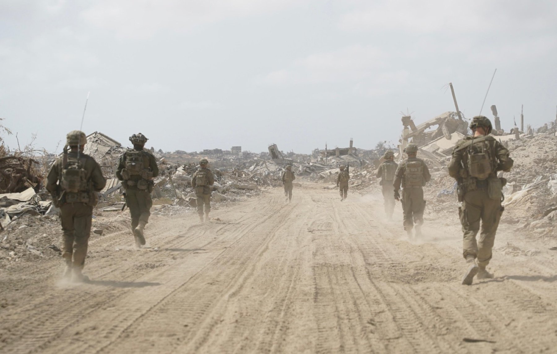 Des soldats marchent sur un chemin poussiéreux, entourés de débris et de ruines.