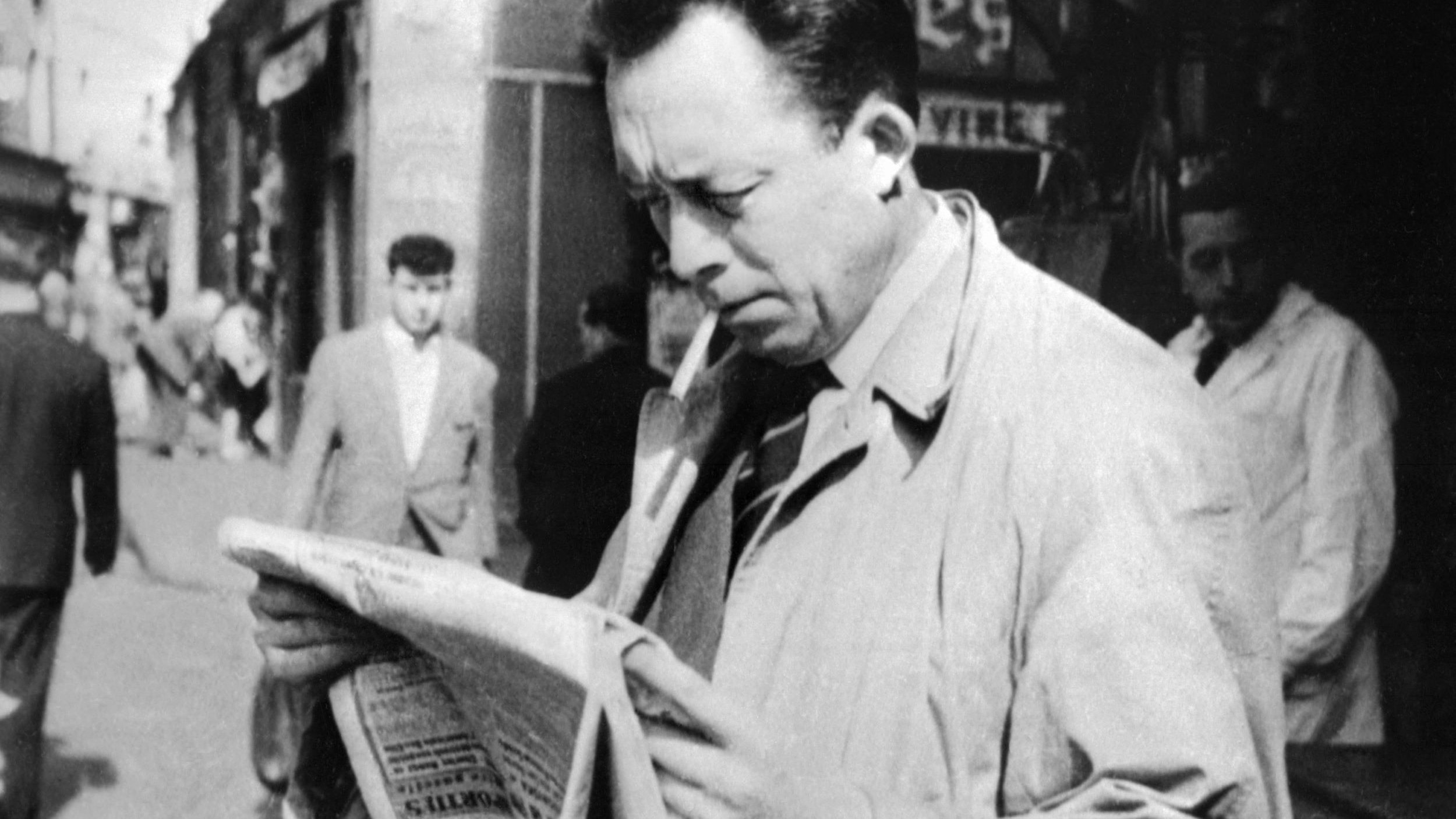 L'image représente un homme dans une rue animée, semblant lire un journal avec attention. Il porte un manteau clair et une cigarette à la bouche. En arrière-plan, on peut voir d'autres passants et des commerces, ce qui donne une ambiance des années passées. La scène évoque une atmosphère de réflexion et d'intérêt pour l'actualité.