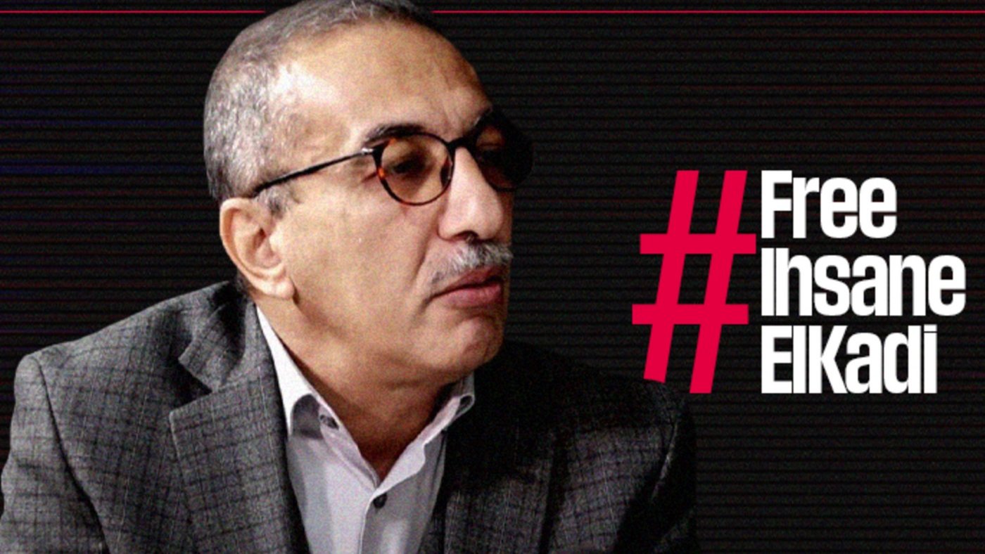 L'image montre un homme portant des lunettes et un costume à carreaux. Il semble participer à une interview ou à un débat, étant tourné vers un interlocuteur. À côté de lui, le texte en gras indique "#Free Ihsane ElKadi", suggérant qu'il est lié à une campagne de sensibilisation ou de soutien pour cette personne. L'arrière-plan présente un design graphique sobre, probablement pour mettre en avant le message.
