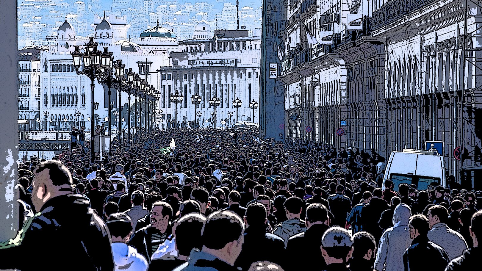 L'image montre une foule dense de personnes marchant dans une rue, probablement dans une ville animée. Les bâtiments sur les côtés semblent historiques, avec une architecture riche. On peut voir des lampadaires le long de la promenade, et au loin, on aperçoit des collines ou des montagnes qui ajoutent à la profondeur de la scène. L'atmosphère semble vibrante et dynamique, reflétant probablement une manifestation ou un événement public.