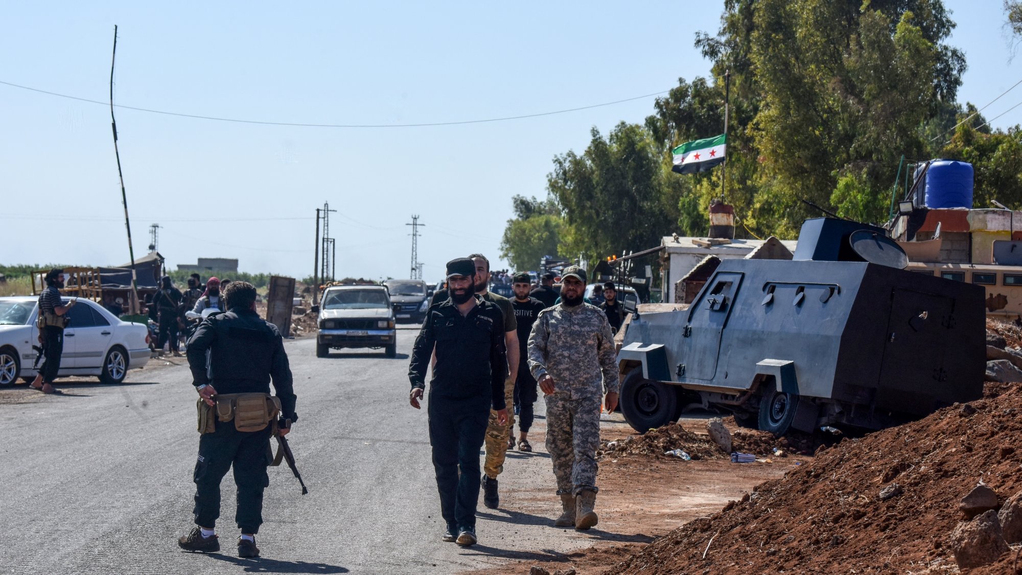 Des soldats marchent le long d'une route, près de véhicules militaires et d'arbres.