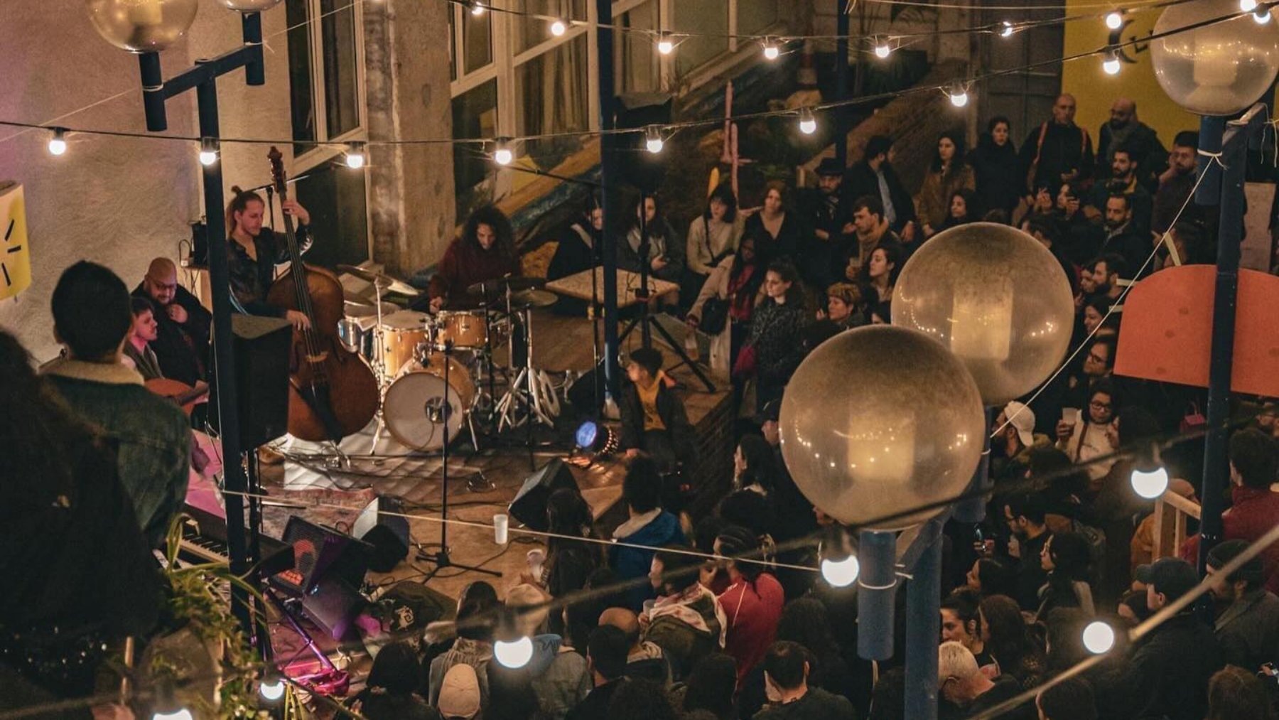 Concert animé dans un lieu chaleureux, éclairé par des guirlandes lumineuses.