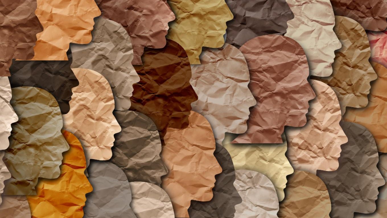 L'image représente une mosaïque de profils humains en silhouettes, créés à partir de papier froissé aux différentes nuances de couleurs de peau. Les teintes varient du beige clair au brun foncé, illustrant la diversité des origines humaines. La texture froissée ajoute une dimension tactile à l'œuvre, suggérant une approche artistique qui évoque à la fois l'unité et la diversité.