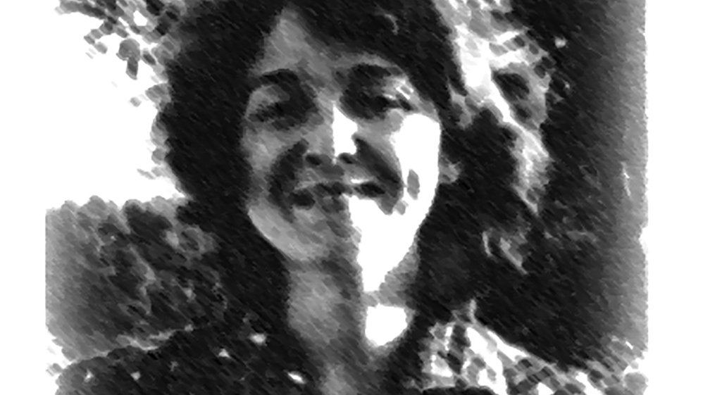 L'image montre une femme avec des cheveux bouclés et un sourire chaleureux. Elle porte une chemise à motifs. L'arrière-plan est flou, suggérant un environnement naturel. L'effet visuel donne une impression de dessin en noir et blanc, ajoutant une touche artistique à la scène.