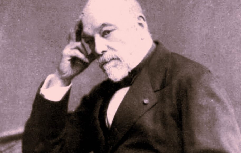 L'image montre un homme mature assis, avec une expression pensive. Il porte un costume sombre et une cravate. Sa main droite touche son menton, ce qui donne une impression de réflexion. Le fond est sombre, ce qui fait ressortir le personnage. La photographie a un style ancien, typique des portraits du 19ème siècle.