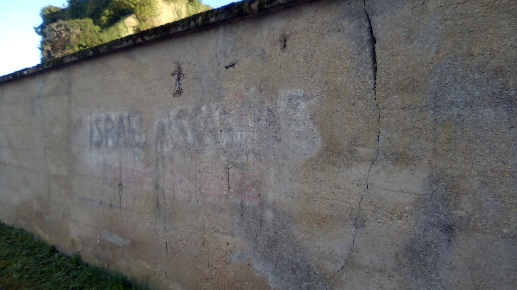 Mur en béton avec des inscriptions effacées et des fissures, sous un ciel bleu.