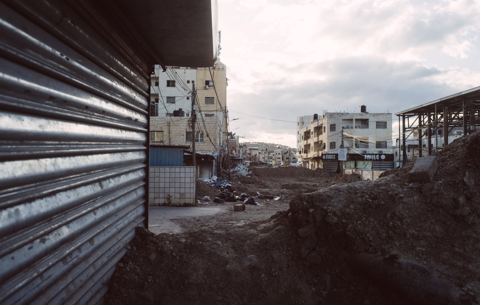Vue d'une rue déserte avec des bâtiments et des gravats, ciel nuageux en arrière-plan.